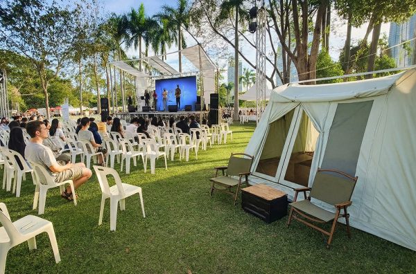 Outdoor camping tent set up beside an open-air event stage on a grass field, showcasing a campsite display scene.