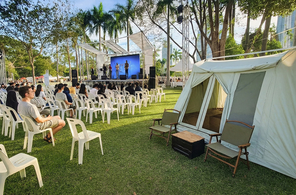 Outdoor camping tent set up beside an open-air event stage on a grass field, showcasing a campsite display scene.