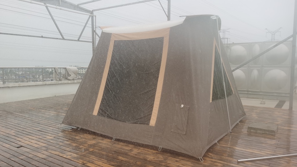 Nastocamp canvas cabin tent undergoing heavy rain and waterproof performance testing on an outdoor factory platform.