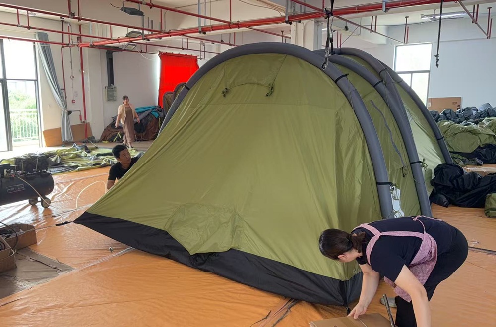 Workers adjusting a large tent set up inside a manufacturing workshop